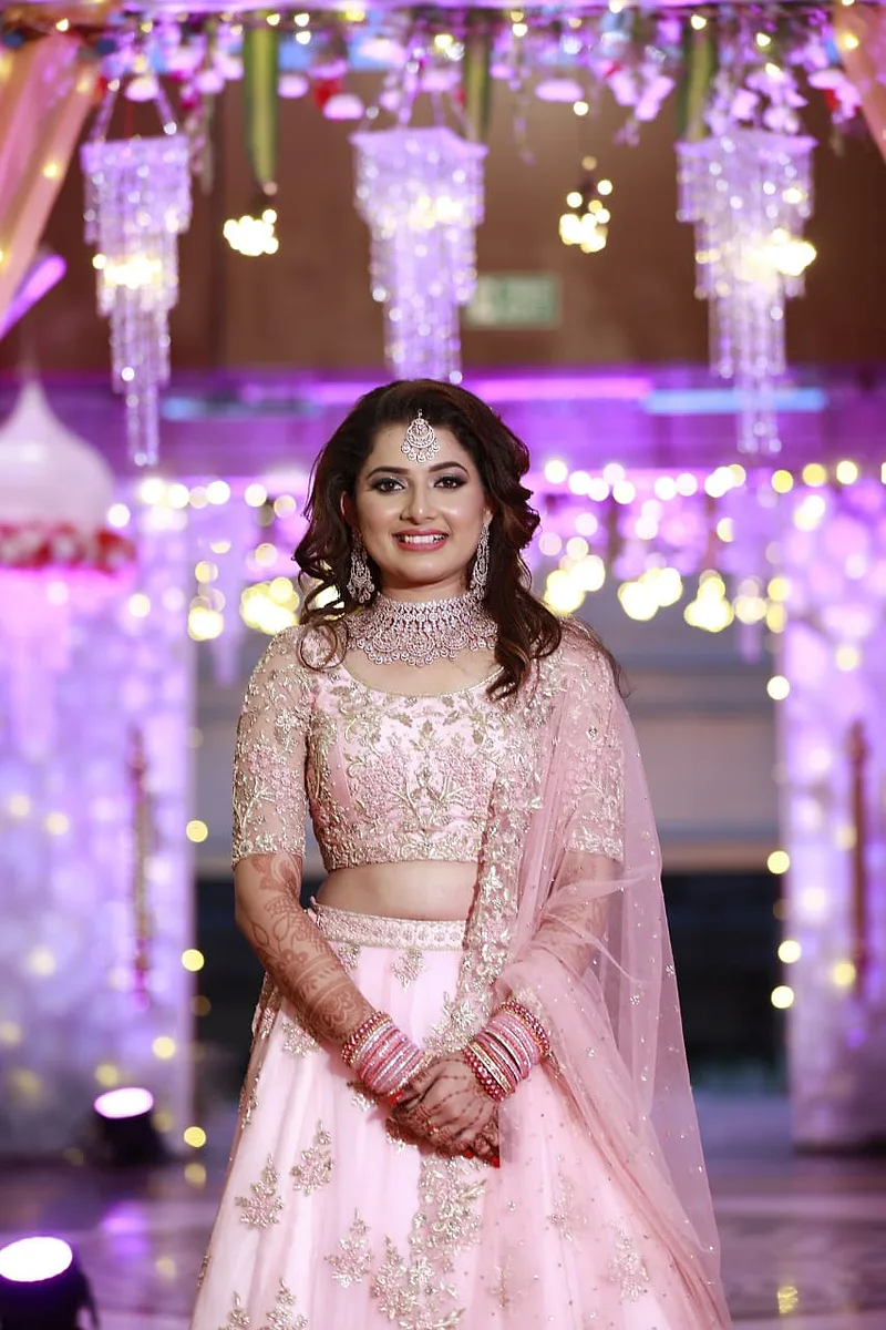 Bride with soft glam makeup and pink lehenga adorned with intricate embroidery.