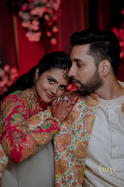 Bride with intricate mehendi and colorful embroidered outfit leaning on groom.