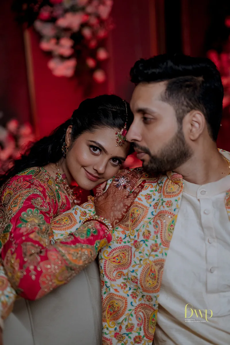 Bride with intricate mehendi and colorful embroidered outfit leaning on groom.