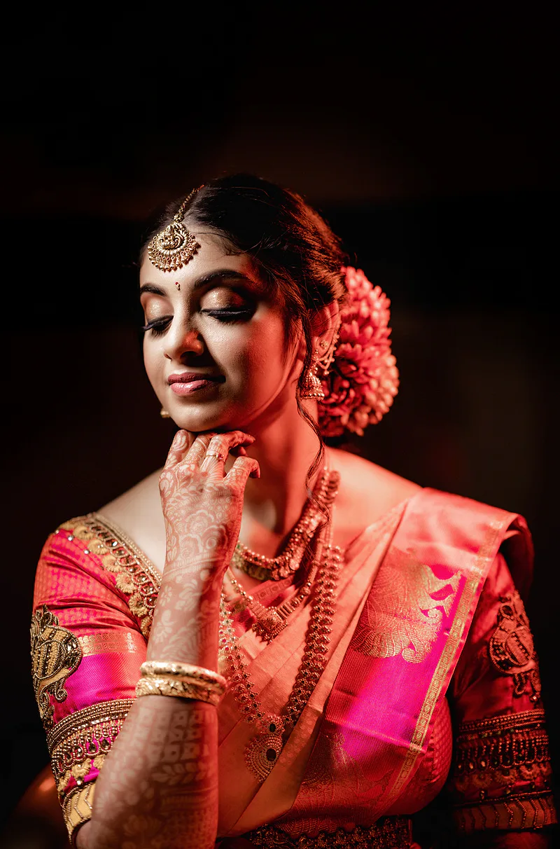 Bride with intricate henna, traditional jewelry, and a pink silk saree.