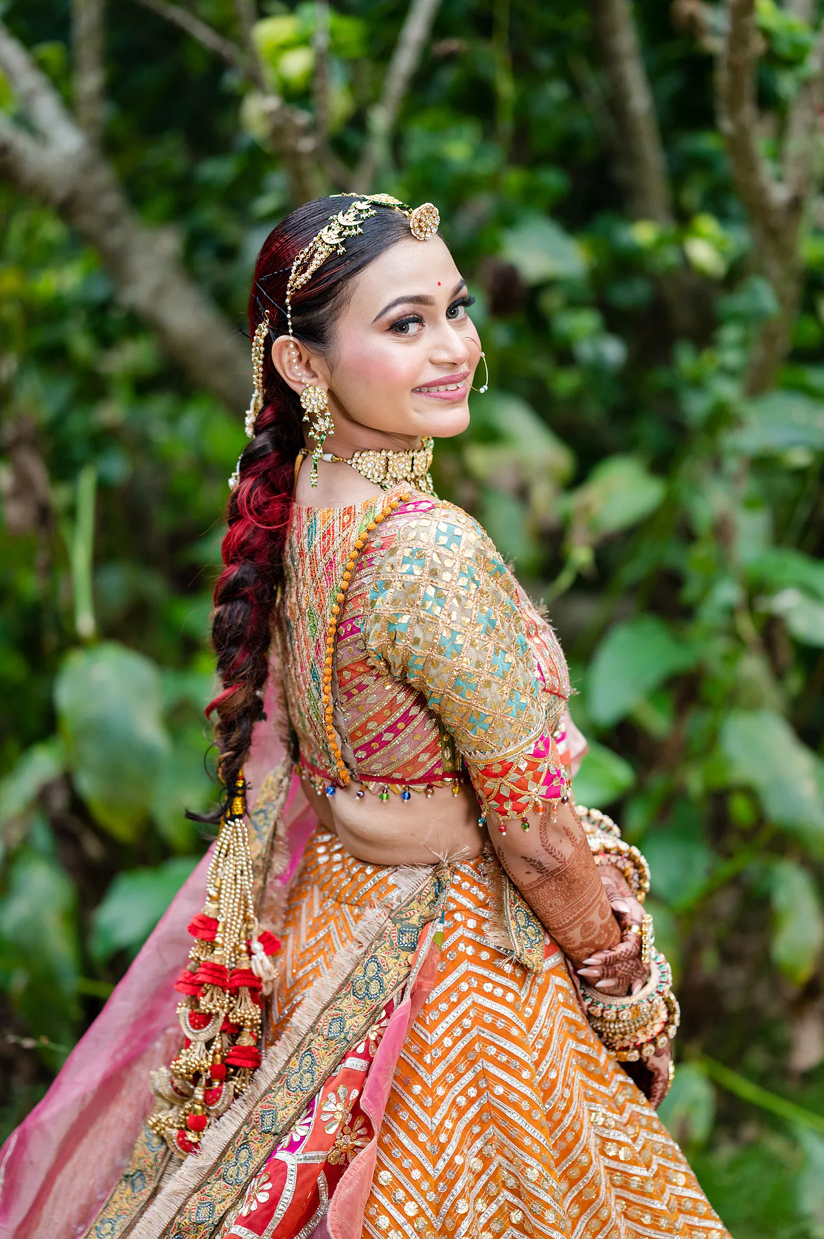 Top Bridal Makeup Artist In Bangalore | Dejavu Makeup by Vinni Bride with intricate braid and colorful lehenga, smiling over her shoulder.