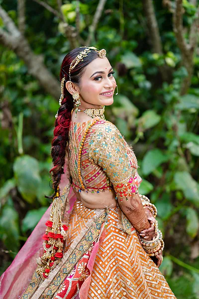 Bride with intricate braid and colorful lehenga, smiling over her shoulder.